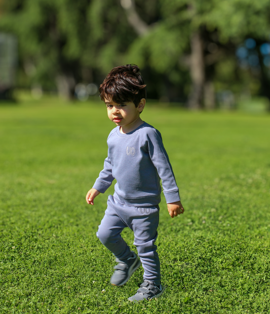 Child in a gray outfit standing on grass with trees in the background